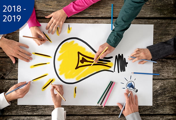 image: Hands around a table drawing a lightbulb on paper