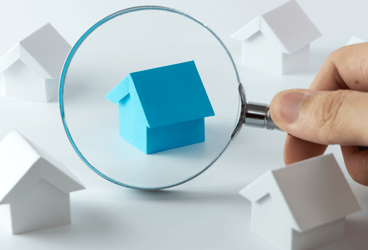 image: hand holding a magnifying glass, examining a symbolic house (AdobeStock)
