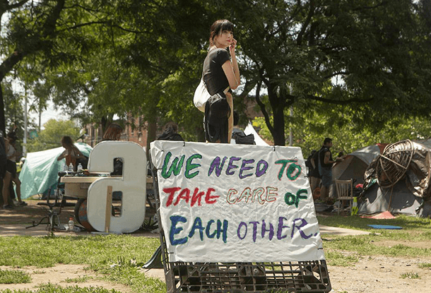 photo: Diana with sign that reads "We need to take care of each other"