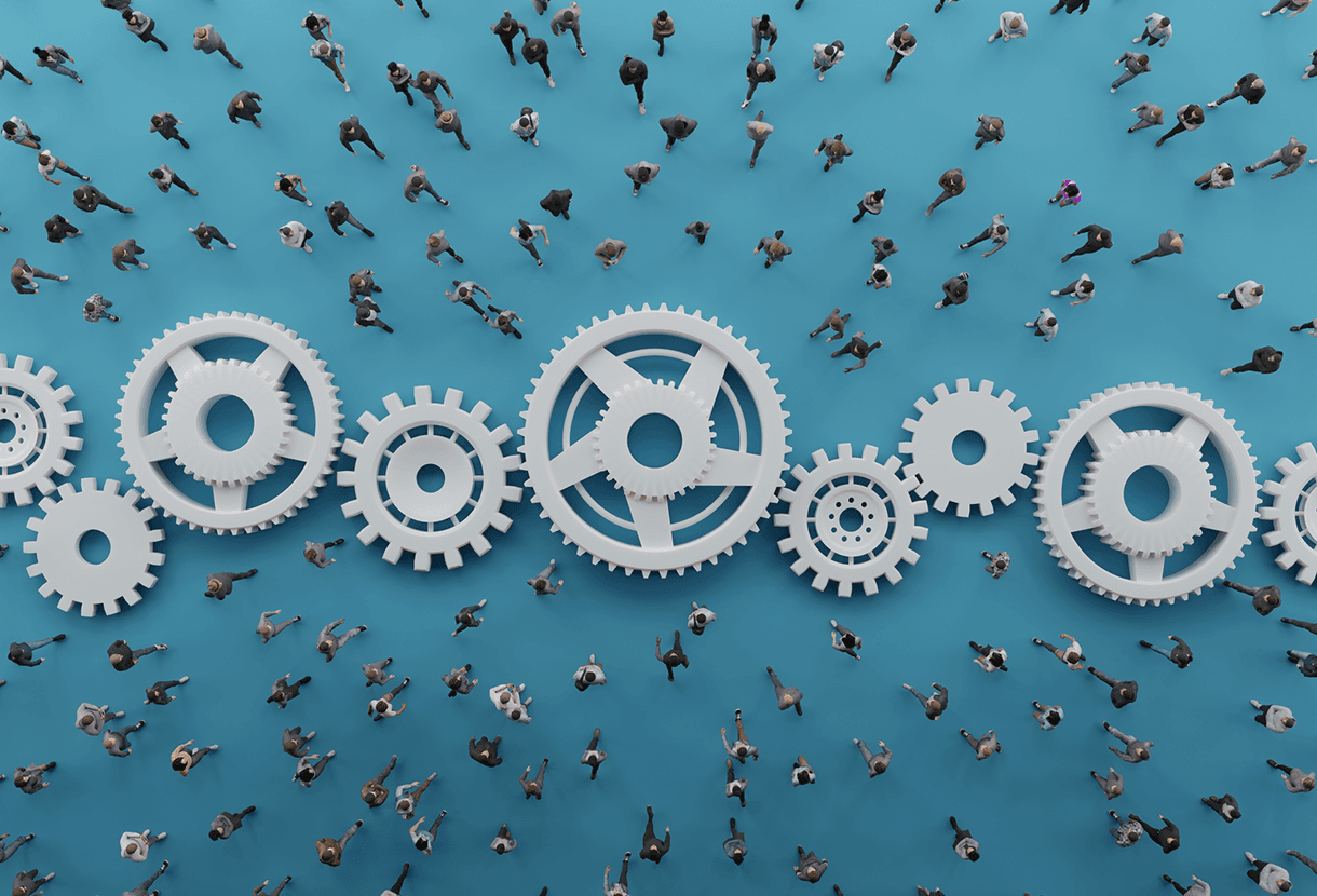image: a bird's-eye view of human figures walking around giant interlocked cogs, symbolizing a system at work (iStockphoto)